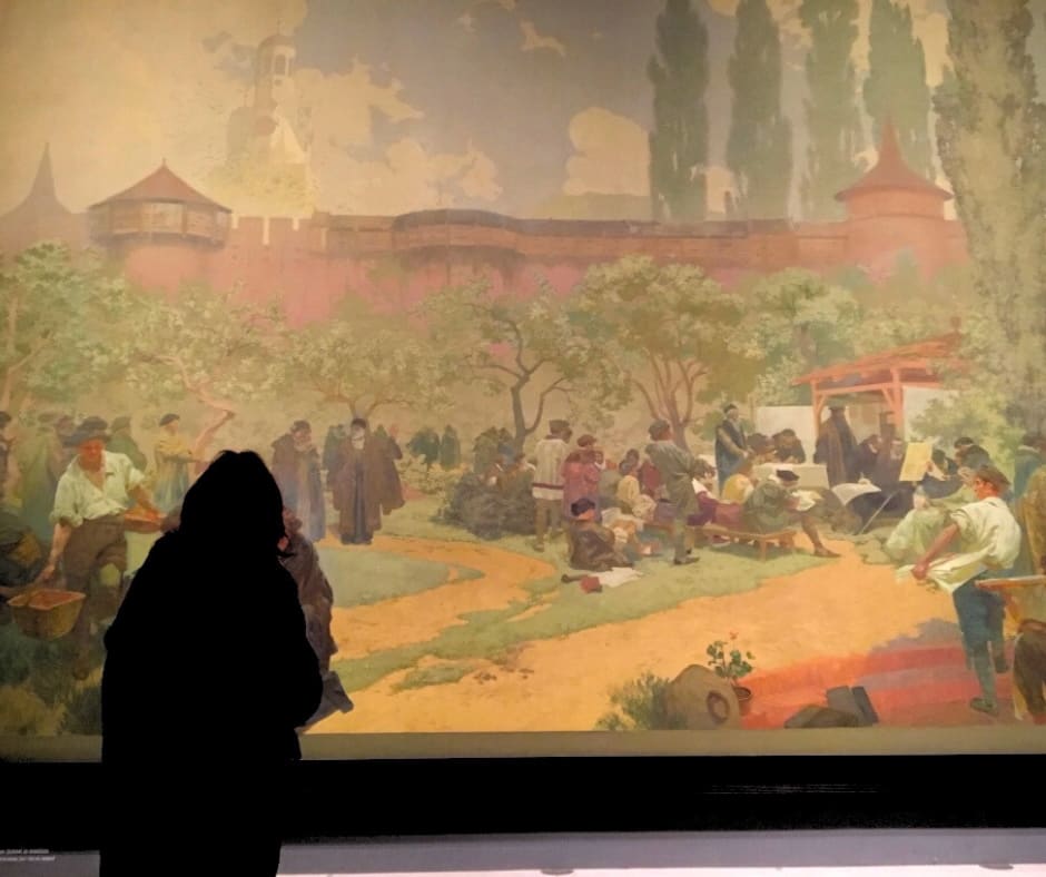 Woman experiencing Mucha's Czech history murals depicting how art preserves cultural identity through historical upheaval